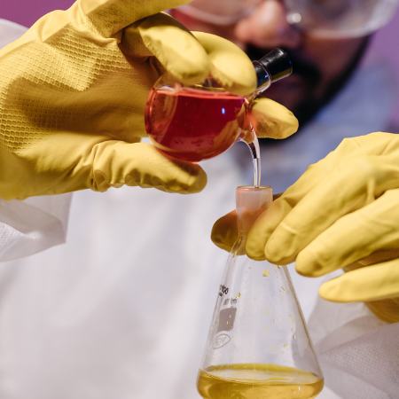 A chemist in protective gear mixes solutions.