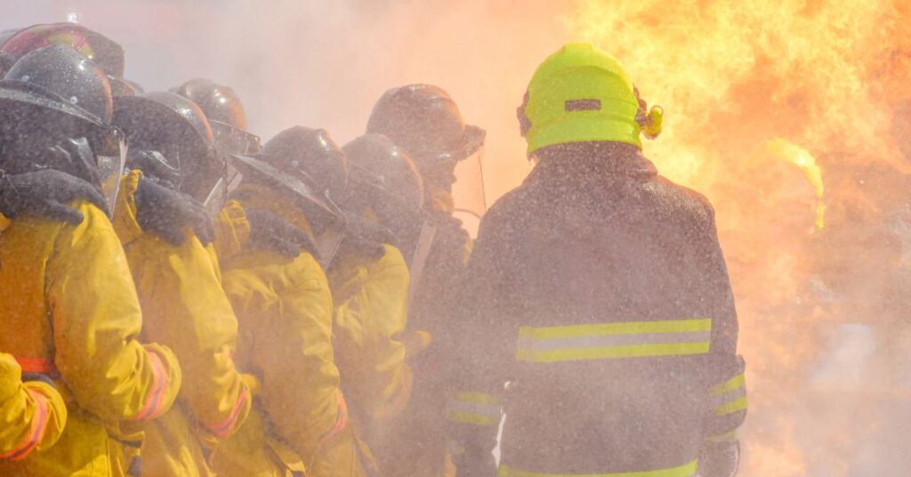 A group of firefighters stand poised to take on a raging fire.
