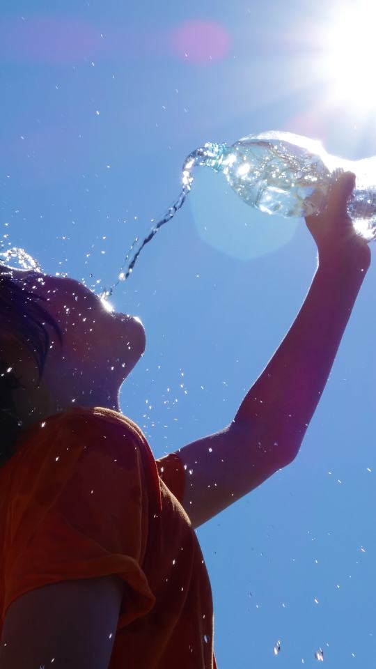 Woman pouring water into her mouth on a bright sunny day.