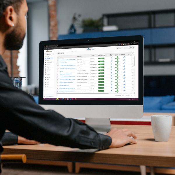 A man sits facing a desktop computer. On the computer screen is the Red2Green healthier materials product library and project management platform from Materially Better.