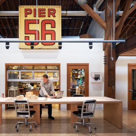 Interior view of Pier 56 Office Renovation, Mithun Architects (Seattle, Washington). A man is seen standing alone at a meeting workstation with offices behind him.