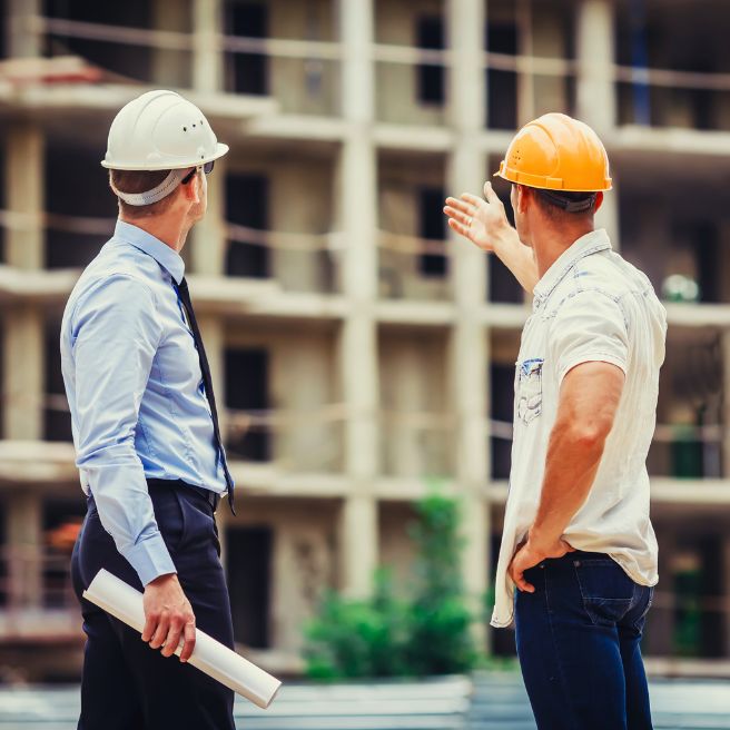Two construction professionals stand in front of a housing project discussing details.