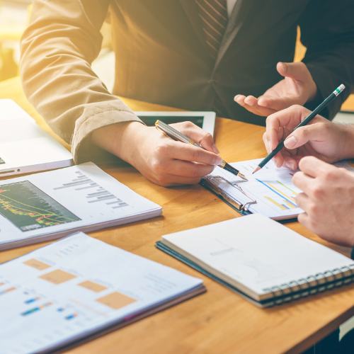 Two people sit at a workstation going over reports and graphs.