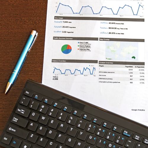 A computer keyboard, materials report, and pen rest on a computer desk.