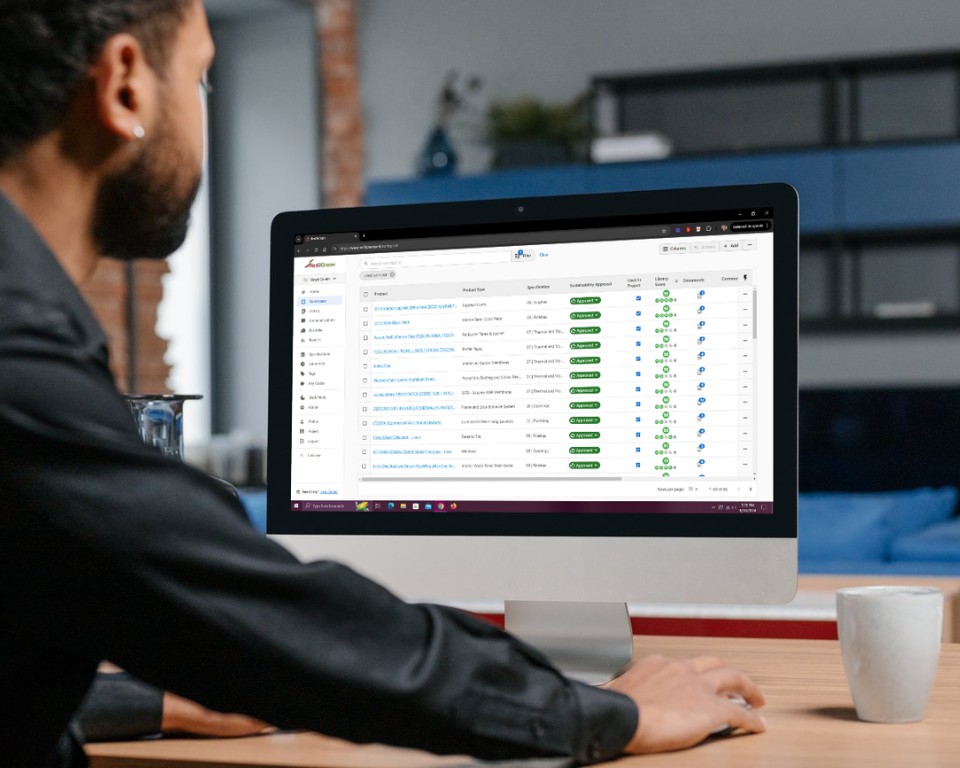 image: man sits at computer display looking at the Red2Green Healthy Materials Product Library and Project Management Workflow platform