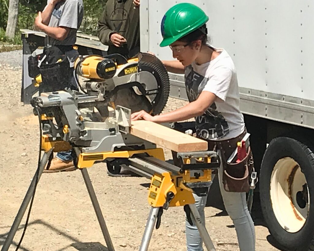 Student from Greater New Bedford Vocational Technical High School cuts wood on a circular saw, preparing it for the Lloyd Center Welcome Center project